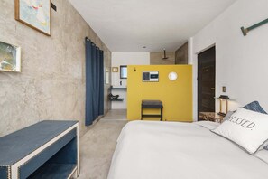 Ett hotellrum med en säng, ett skrivbord, en stol, ett litet bord, en spegel, ett fönster och en dörr.