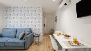 Ett modernt vardagsrum med en blå soffa, ett litet runt bord och en matplats med ett vitt bord och stolar.