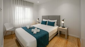 Ett modernt hotellrum med en stor säng, två sängbord, en stol och ett fönster med tunna, genomskinliga gardiner.