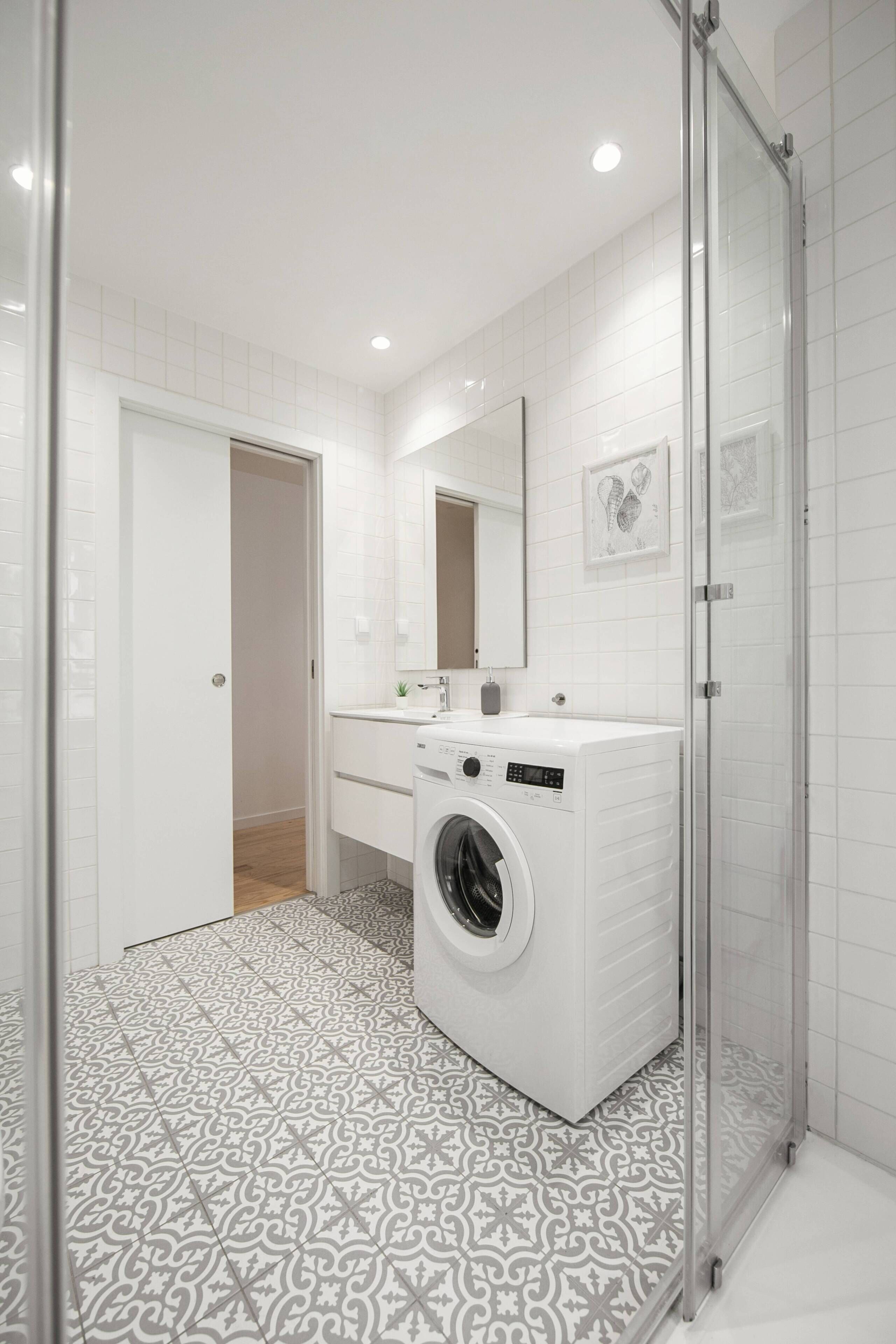 A modern bathroom with a washing machine, a glass shower enclosure, and patterned floor tiles.