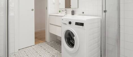 A modern bathroom with a washing machine, a glass shower enclosure, and patterned floor tiles.