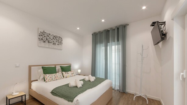 Ein modernes Schlafzimmer mit einem hölzernen Bett, grün-weißen Kissen, einer grünen Tagesdecke und einer Stehlampe.