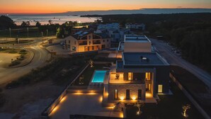 A modern residential area with a swimming pool, multiple houses, and a view of the sea at sunset. - Awesome home in Funtana (Funtana)