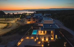 Ein modernes Wohngebiet mit Schwimmbad, mehreren Häusern und Blick auf das Meer bei Sonnenuntergang.