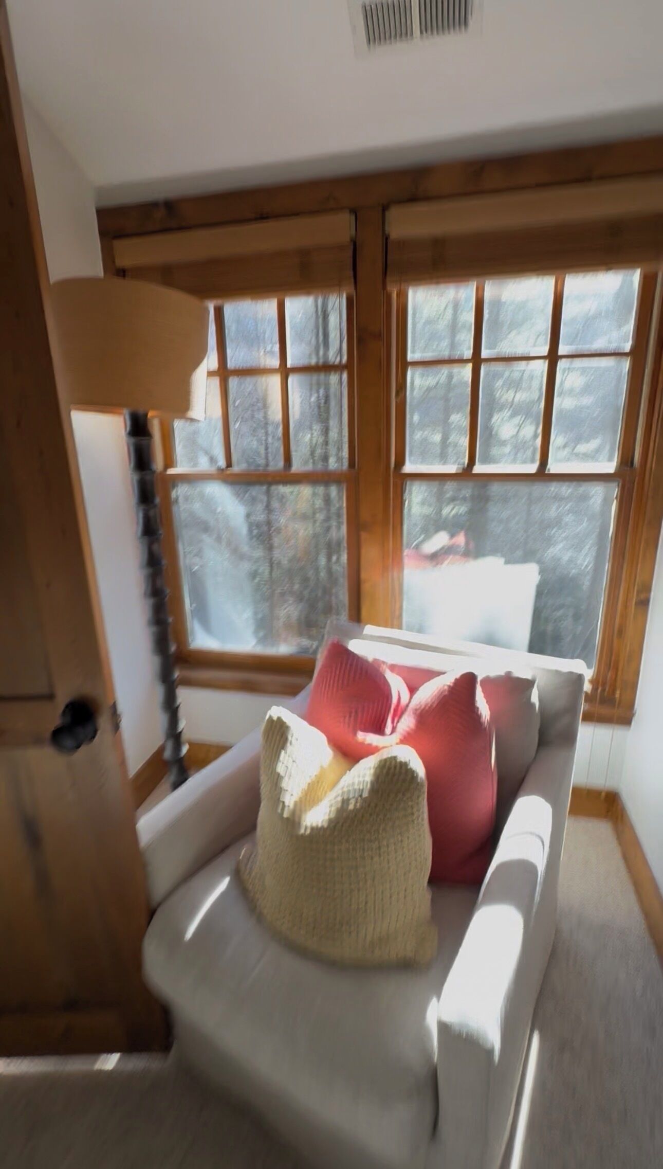 A cozy room with a white sofa, a knitted throw, and a window with a view of trees.