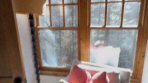 A cozy room with a white sofa, a knitted throw, and a window with a view of trees. - Cashiers, Trillium Lake Glenville Mountain Home 2 bedroom plus kids bunk room (Cashiers)