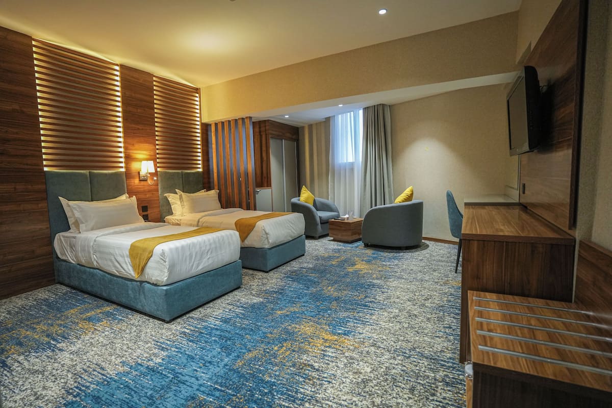 Habitación de hotel con dos camas, un escritorio, una silla y un televisor.