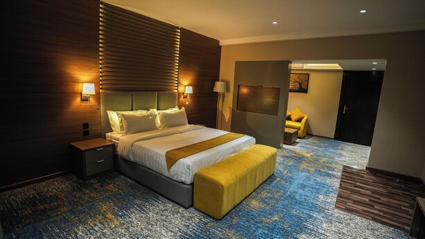 A modern hotel room with a large bed, bedside lamps, a wooden headboard, and a blue carpet. - Haven Plaza Hotel Riyadh  (Riyadh)