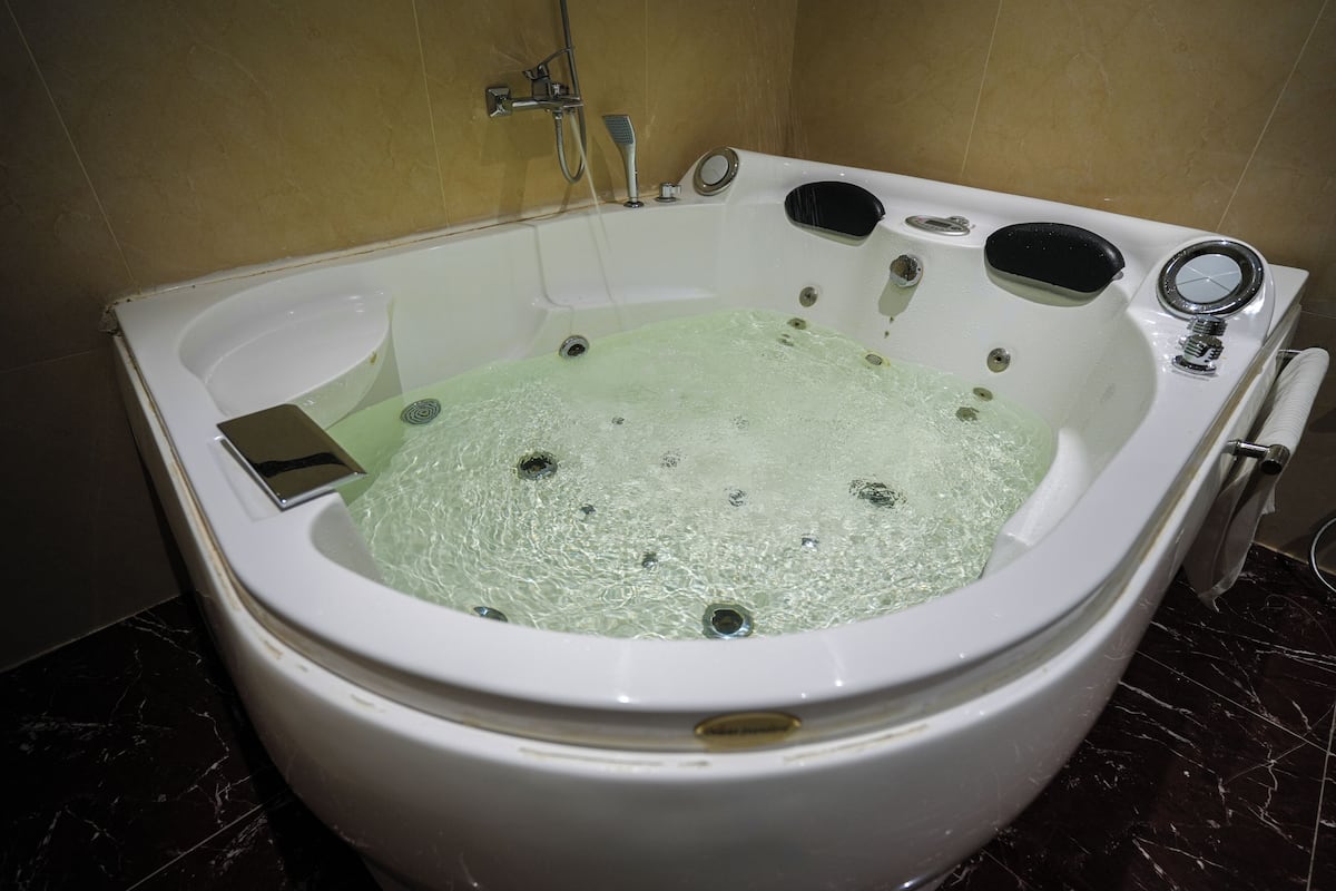 Una bañera blanca con asiento integrado, cabezal de ducha de mano y panel de control.
