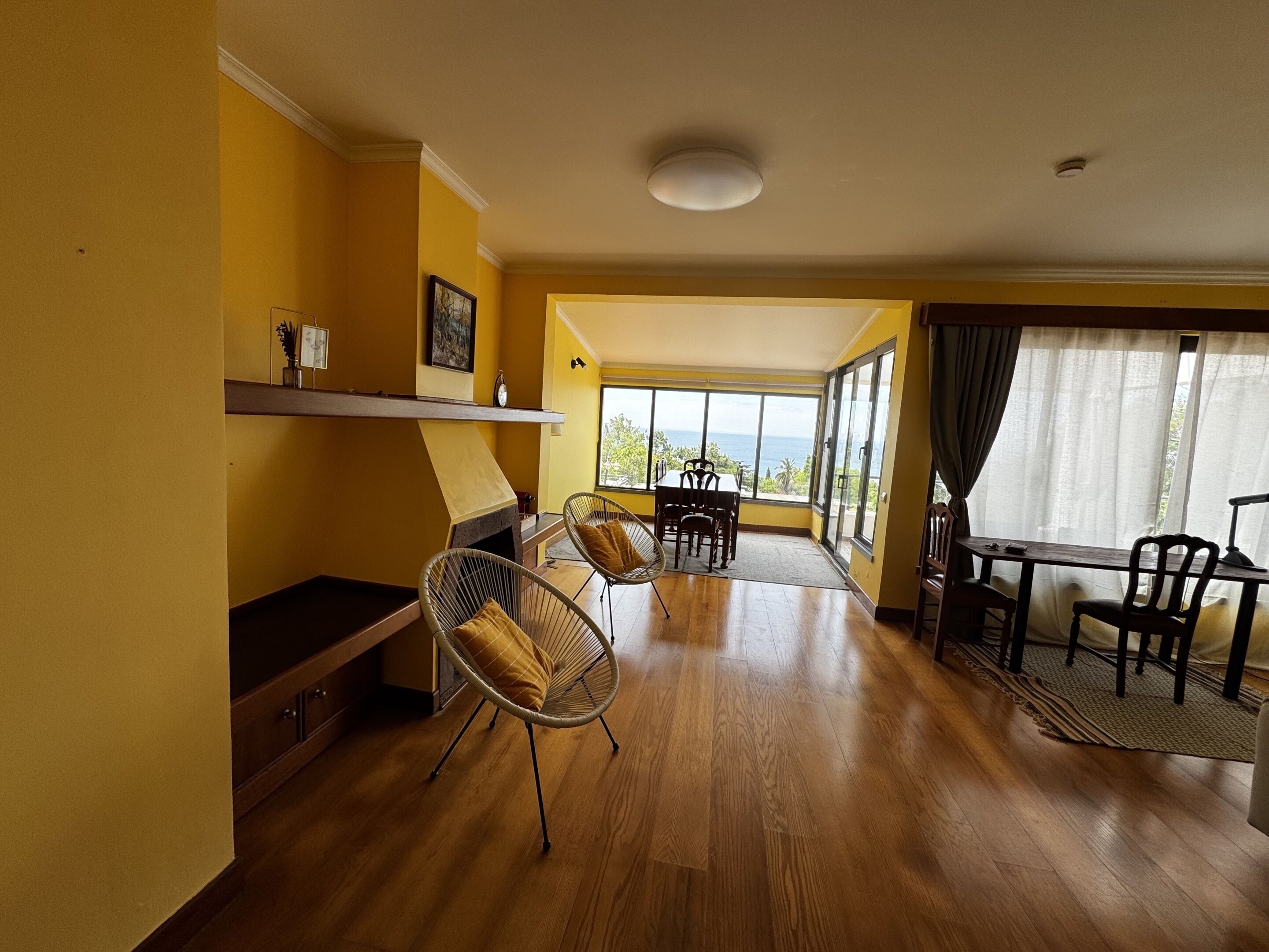 Une pièce dotée d’une cheminée, d’un plancher en bois, d’un coin repas avec des chaises et de grandes fenêtres offrant une vue dégagée.