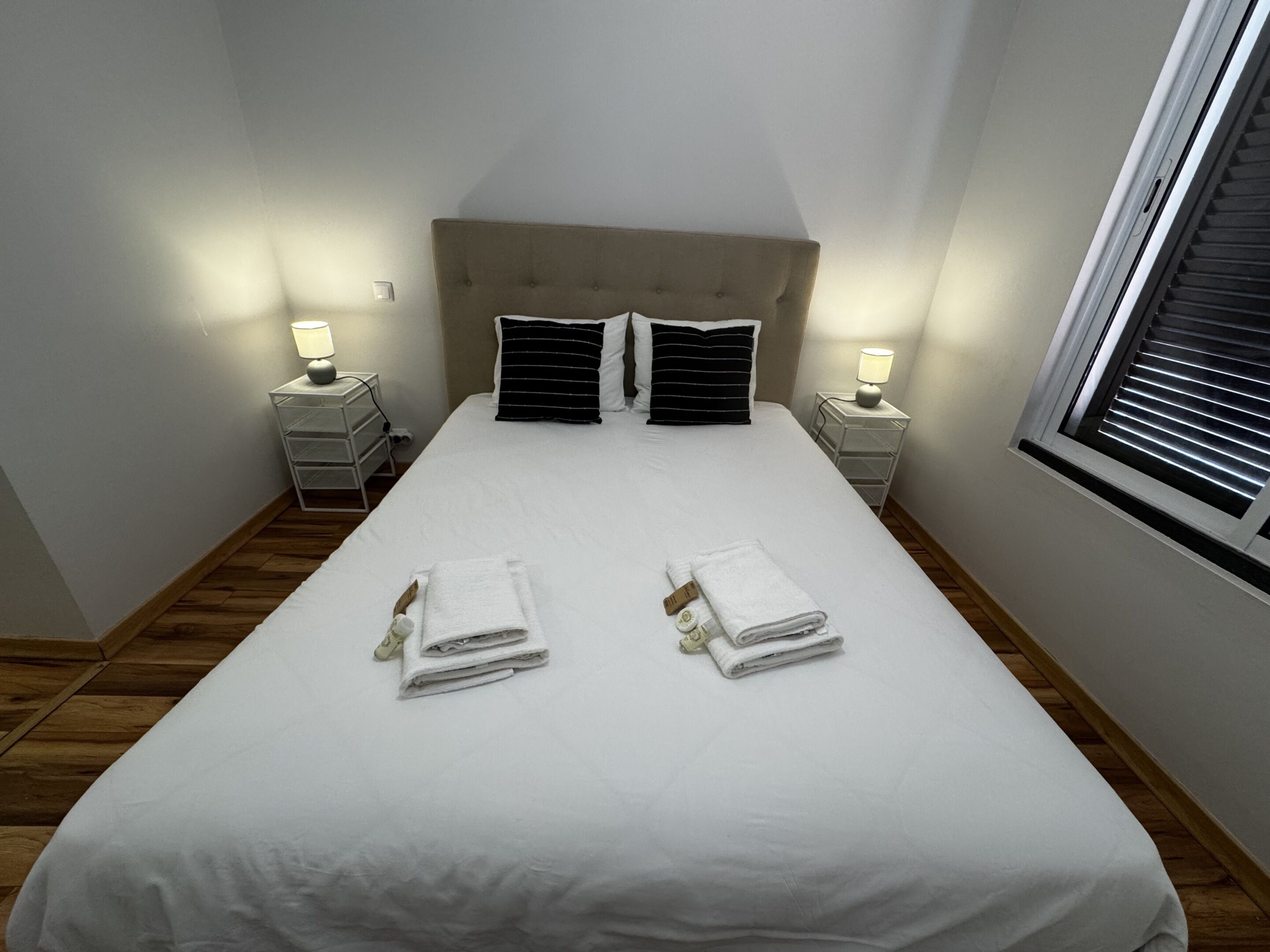 Een netjes opgemaakt bed met witte lakens, twee zwart-wit gestreepte kussens en twee nachtkastjes met lampen.