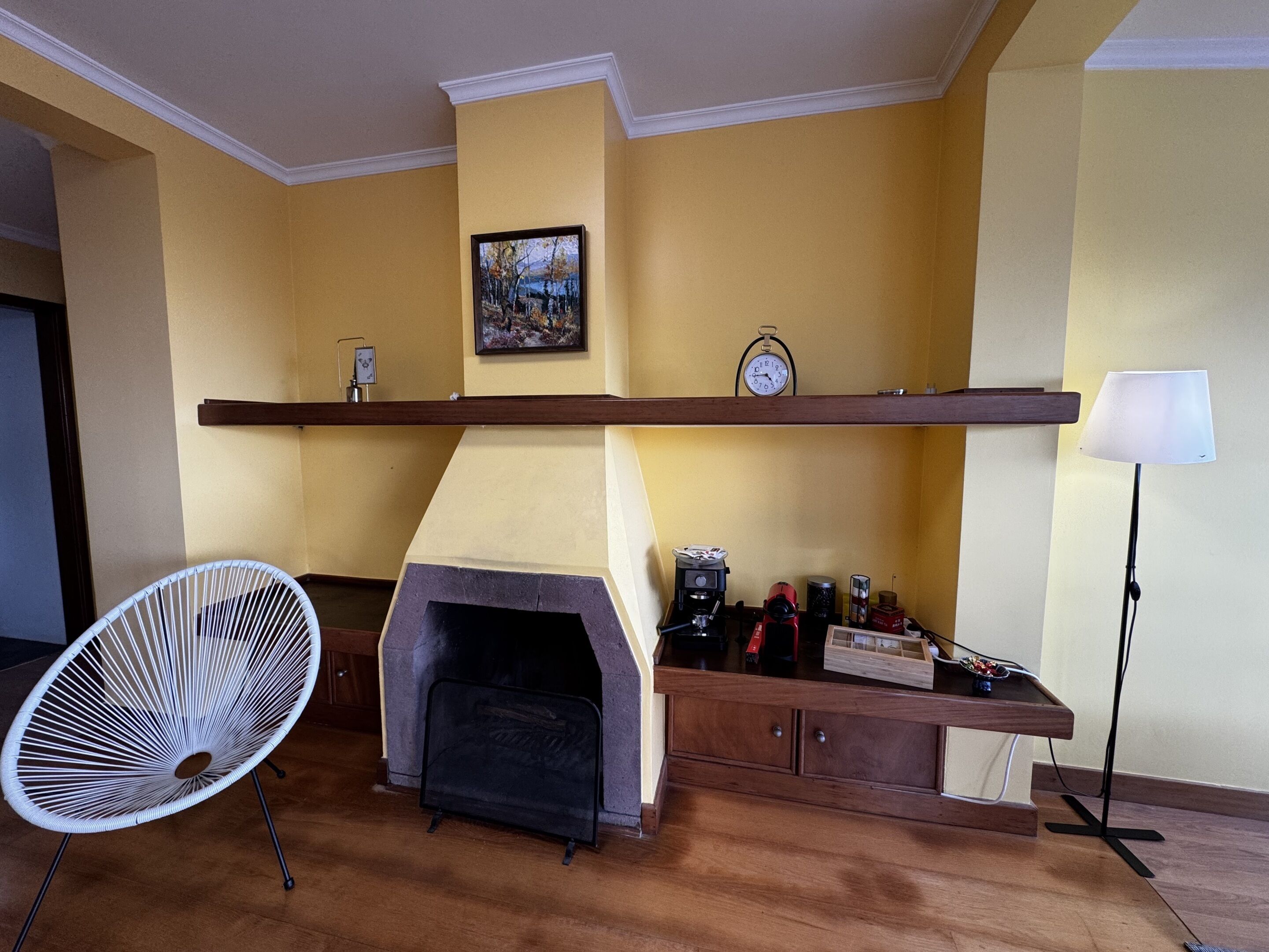 A living room with a fireplace, a fan, and a shelf with various items.