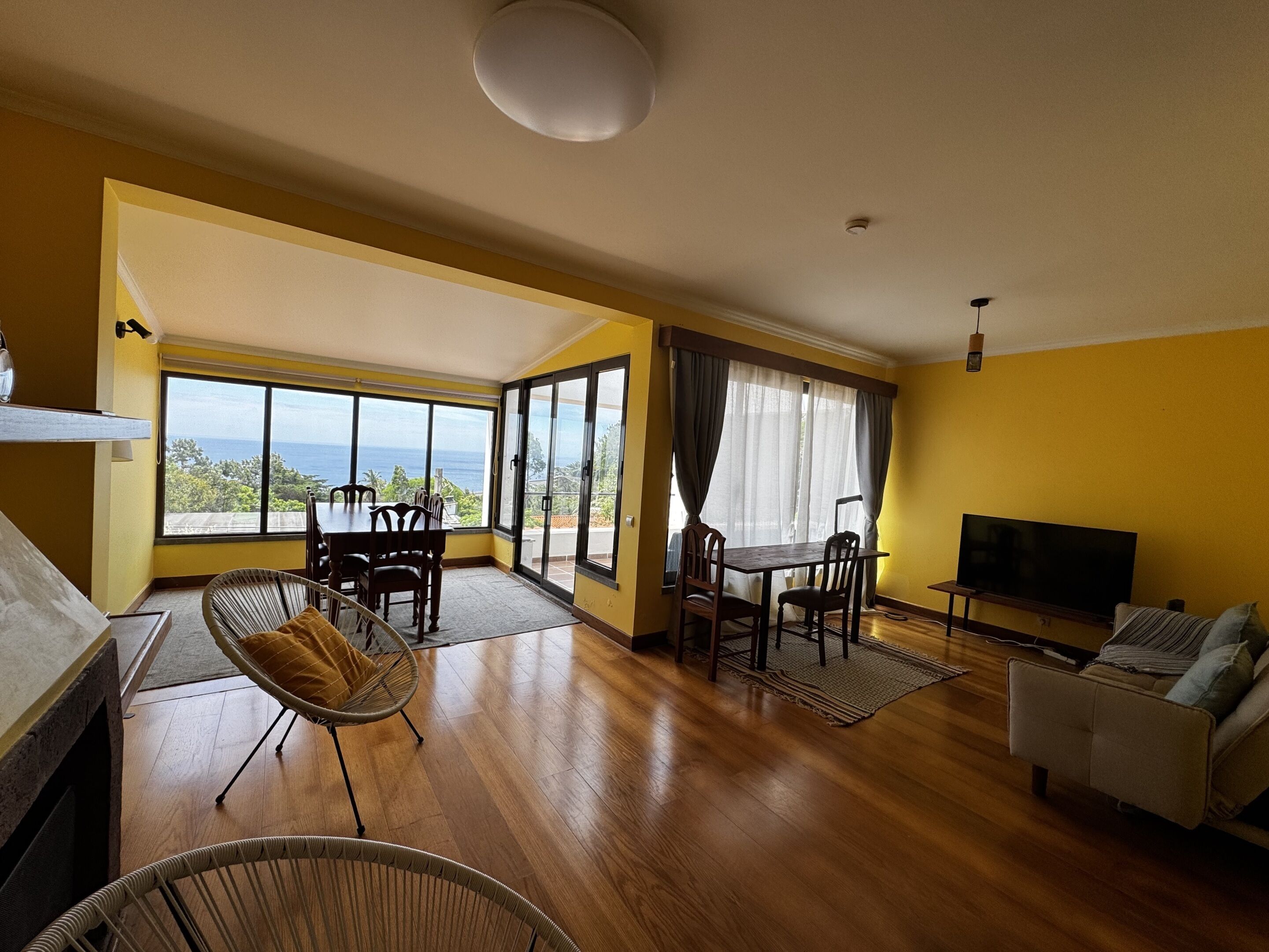 A spacious living room with a large window, a dining area, a sofa, and a TV.