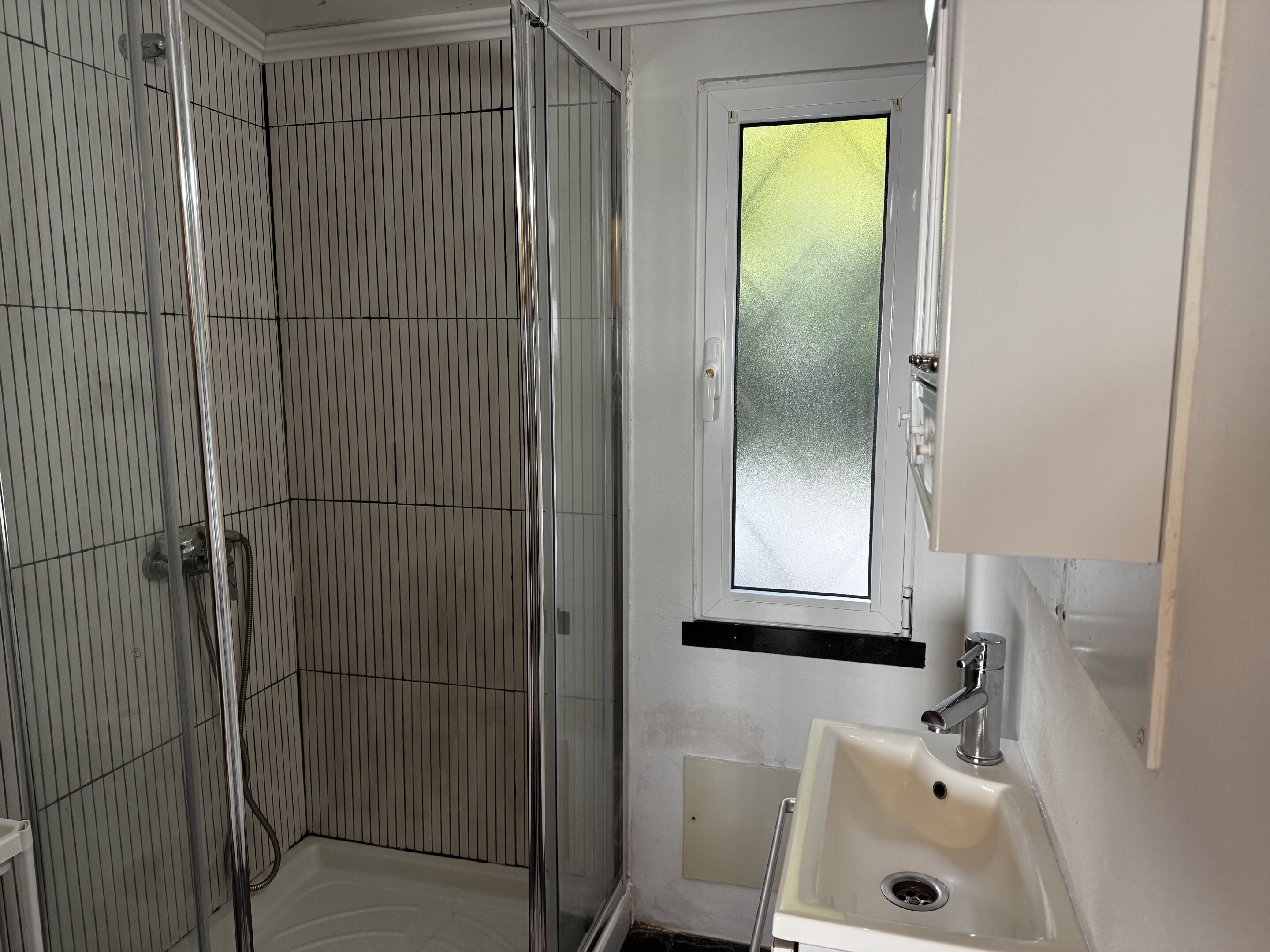 Een badkamer met een douche, een raam en een wastafel.