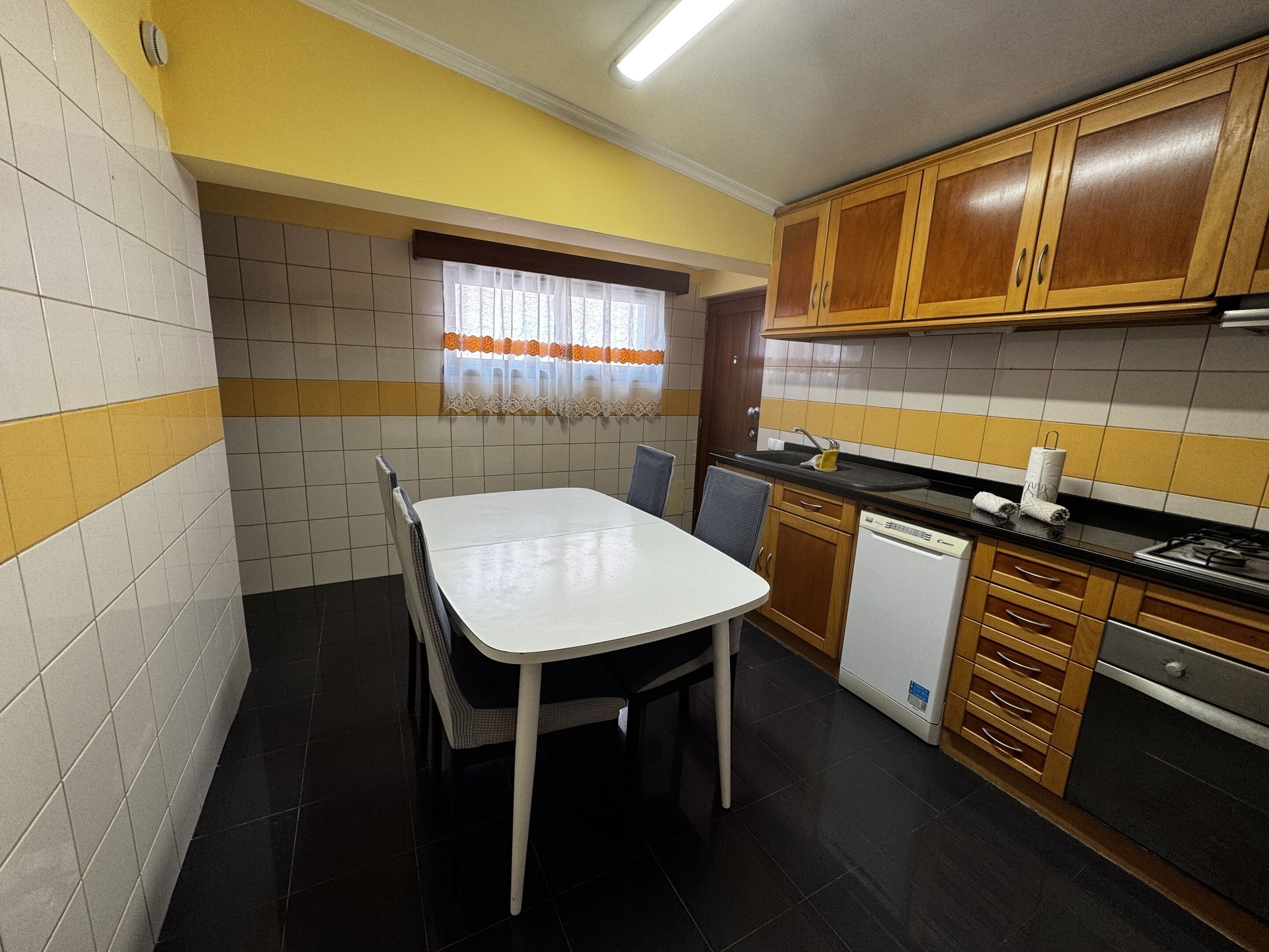 Una cocina con una mesa de comedor, sillas, una ventana con cortinas y armarios de madera.