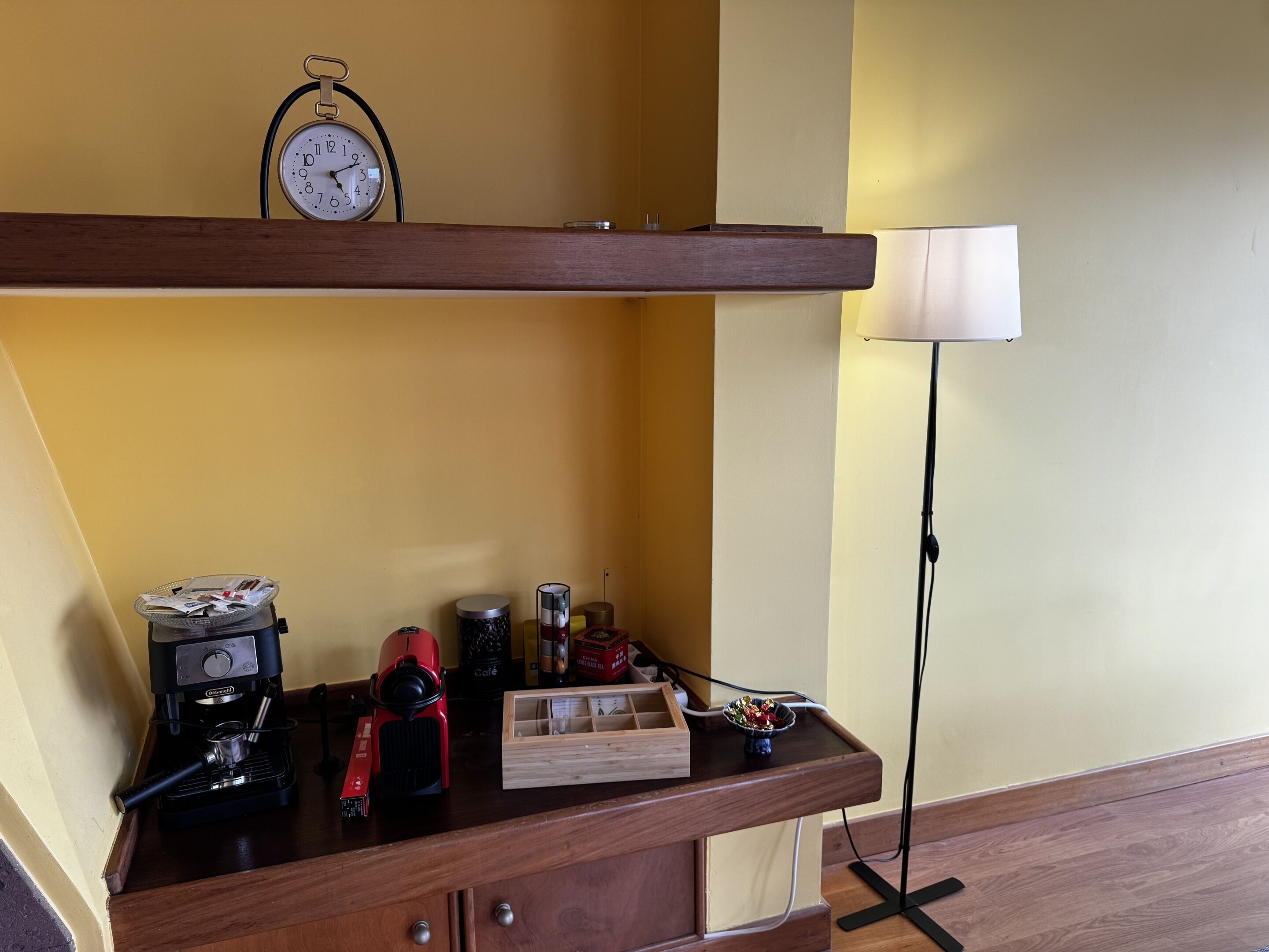 A kitchen counter with a coffee machine, a red kettle, a basket of papers, and a small wooden box.