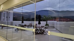 Ein moderner Büroarbeitsplatz mit Glastrennwand, einem runden Tisch mit Stühlen und Blick auf eine Berglandschaft.