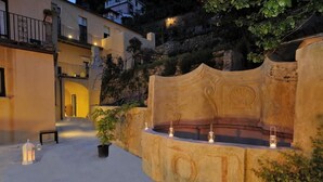 A courtyard with a stone fountain, potted plants, and a bench.