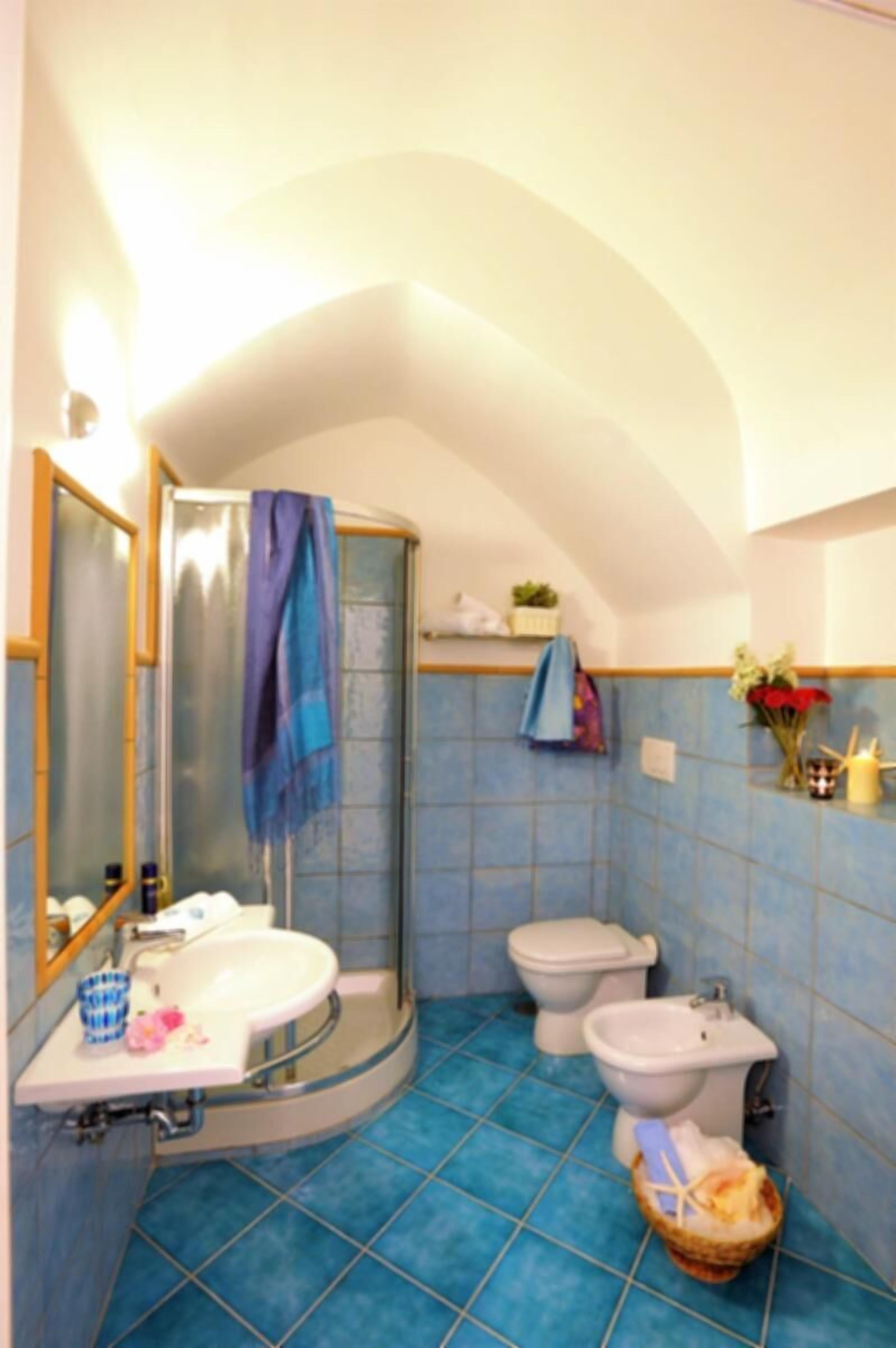 Un baño con un lavamanos curvo, dos bidés, una ducha y suelo de baldosas azules.