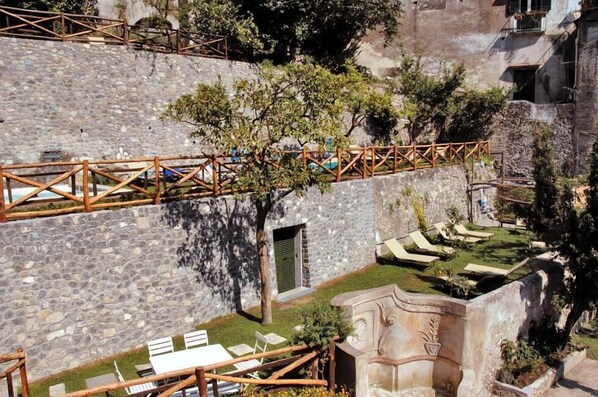Ein Steinhaus mit einer Holzbrücke, Außenbestuhlung und einer Steinmauer.
