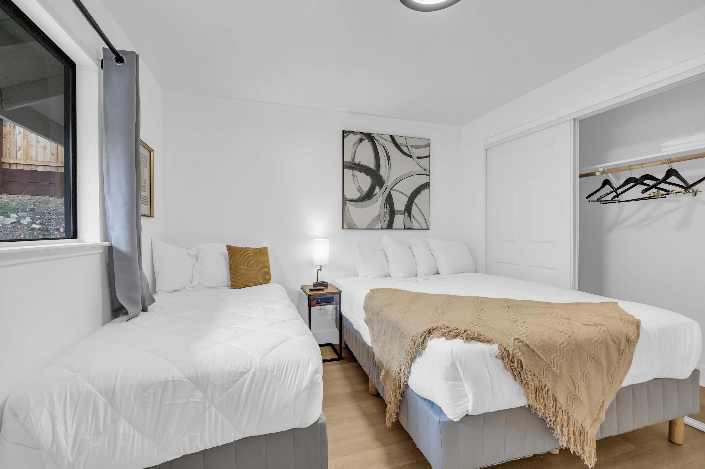 Ein Schlafzimmer mit zwei Betten, einem Nachttisch mit Lampe, einem Wandbild und einem Kleiderständer.