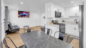 A modern kitchen with white cabinets, a built-in microwave, and a stainless steel refrigerator. There is a dining area with a marble table and black chairs. - Tranquil Oasis Duplex/5Baths/Sleeps 15 (Reno)