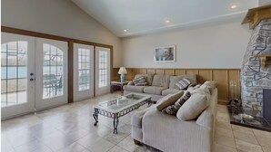 A spacious living room with a high ceiling, a stone fireplace, a large sofa, and a glass coffee table. - Luxury Lake House - Hot Tub - Fire Pit - BBQ -Dock (Hasting)