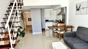 Eine moderne Wohnung mit Treppe, Essbereich, grauem Sofa und einer Küche im Hintergrund.
