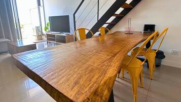 Un comedor espacioso con una larga mesa de madera, sillas amarillas, un televisor y una escalera.