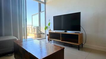 Una sala de estar con televisor de pantalla plana, una mesa de centro de madera y un ventanal con cortinas.