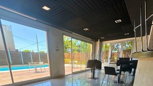 A spacious indoor area with a pool visible through large windows, modern furniture, and a clean, tiled floor. - Apartment Alassio 2 rooms (Buenos Aires)