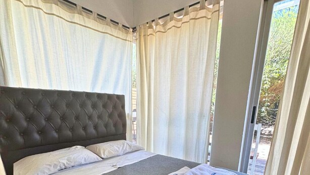 A bedroom with a large bed, a tufted headboard, and a view through the window. - Apartment Alassio 2 rooms (Buenos Aires)