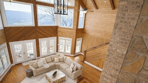 A spacious living room with a large L-shaped sectional sofa, a small coffee table, and a view of the outdoors through large windows. - Panoramic Views at Paul’s Point (Altamont)