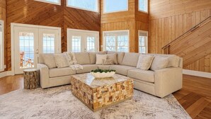 A spacious living room with a large sectional sofa, a wooden coffee table, and a view of the outdoors through large windows. - Panoramic Views at Paul’s Point (Altamont)