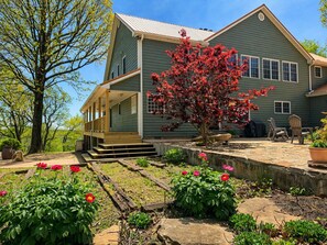 Ein zweistöckiges Haus mit Veranda, Garten mit Blumen und Baum mit roten Blättern.