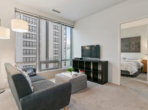 A modern living room with a grey sofa, a coffee table, a TV on a black stand, and a bookshelf. - Bright 1 Bedroom Condo in the Heart of the City! (Vancouver)