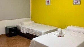 Ein Hotelzimmer mit zwei Betten, einem kleinen Nachttisch, einer Wandklimaanlage und Holzboden.