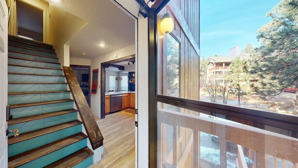 Un interior moderno con una escalera de madera, una zona de cocina y un amplio ventanal con vistas al exterior.