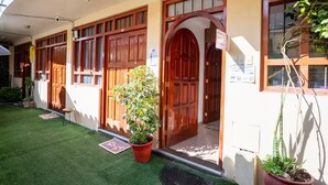 A building with multiple wooden doors and windows, a small garden area with artificial grass, and potted plants. - Family Apartment - - Bed and Breakfast in Cusco (Cusco)
