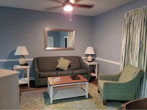 Ein Wohnzimmer mit einer Couch, einem Couchtisch, einem Sessel, einer Lampe und einem Deckenventilator.