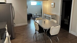 Une cuisine moderne avec une table et des chaises, un réfrigérateur et une fenêtre équipée de stores.