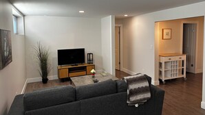 Un salon moderne avec un téléviseur à écran plat, un canapé gris, une table basse et une petite plante.
