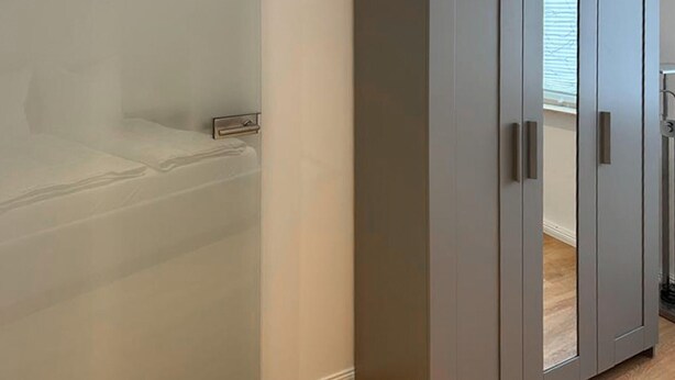 Une chambre avec un lit, une armoire et une fenêtre avec des stores.