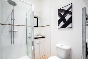 Ein modernes Badezimmer mit Duschkabine aus Glas, weißen Fliesen, einem schwarz-weißen abstrakten Gemälde und einer weißen Toilette.