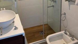 Een moderne badkamer met een douchecabine van glas, een witte wastafel en een toiletbril met douchefunctie.
