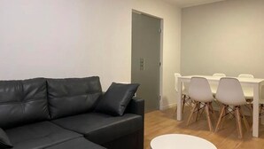 Een moderne woonkamer met een zwarte leren bank, een witte eettafel met stoelen en een houten vloer.
