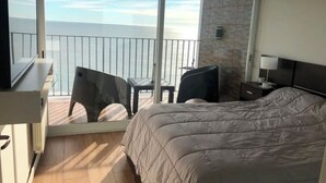 Een hotelkamer met een groot bed, een bureau, een stoel en uitzicht op zee.