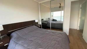 Een slaapkamer met een groot bed, een nachtkastje, een spiegel en een schuifdeur naar een andere kamer.