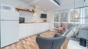 A modern kitchen with white cabinets, a microwave, and a stove. There is a TV mounted on the wall and a window with a view of trees. - Superb views and literally 2 min walk to resort ! (Mont-Tremblant)