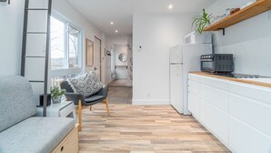 A modern kitchen with white cabinets, a wooden countertop, and a built-in stove. There is a grey sofa with a patterned cushion and a ladder leaning against the wall. - Superb views and literally 2 min walk to resort ! (Mont-Tremblant)